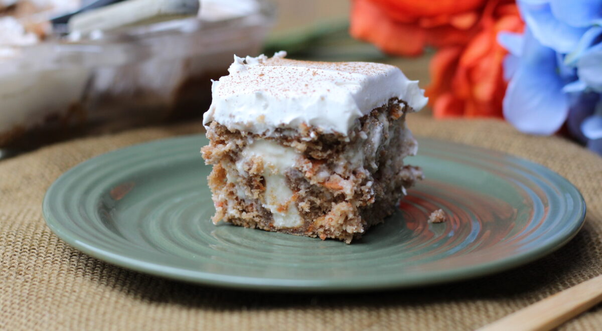 A piece of cake on a green plate, with orange and blue flowers in the background.