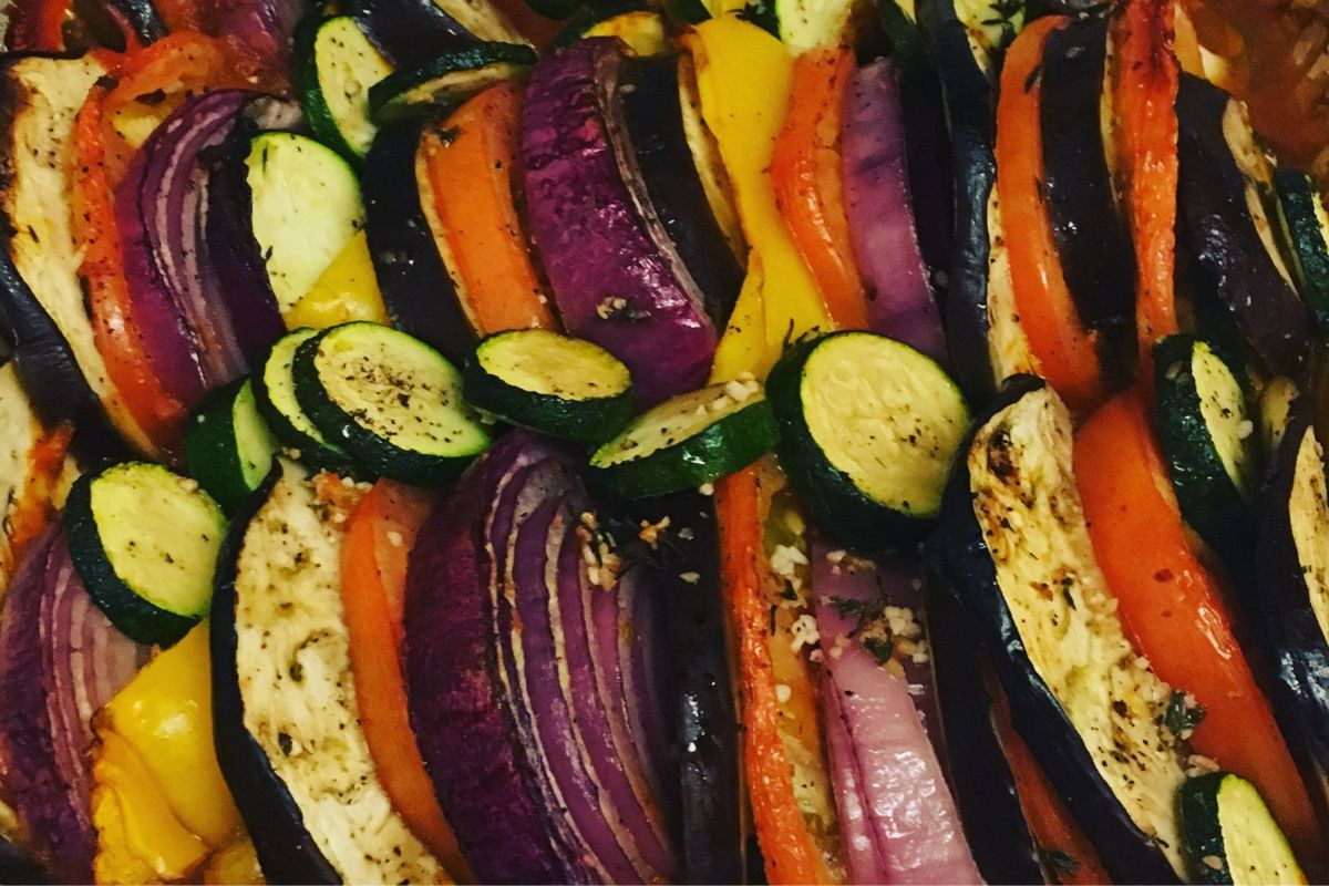 Sliced zucchini, eggplant, red onion, and tomato arranged in rows and seasoned with herbs and spices, ready for roasting.
