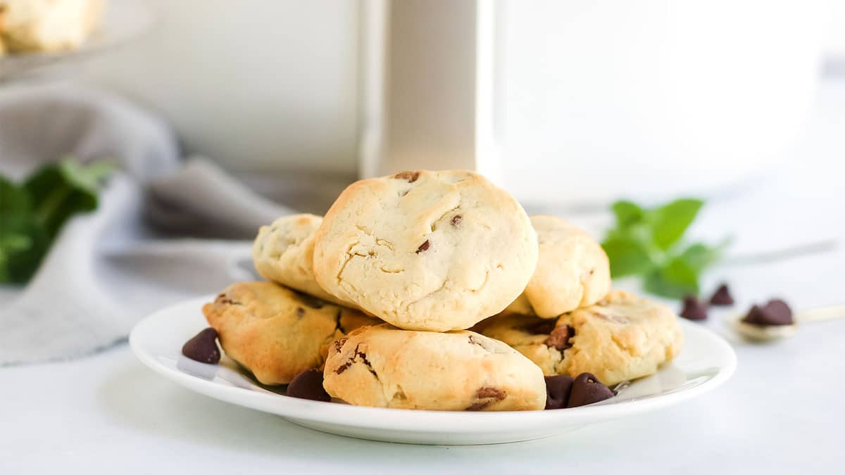 A plate of chocolate chip cookies is displayed on a white surface, with a few chocolate chips scattered around the plateโperfect inspiration for your National Chocolate Chip Cookie Day recipes.