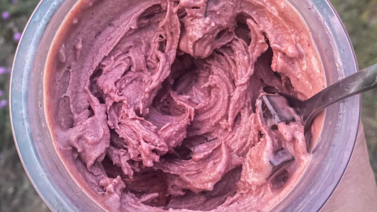 A bowl of thick, purple-colored ice cream or frozen dessert with a metal spoon inside.