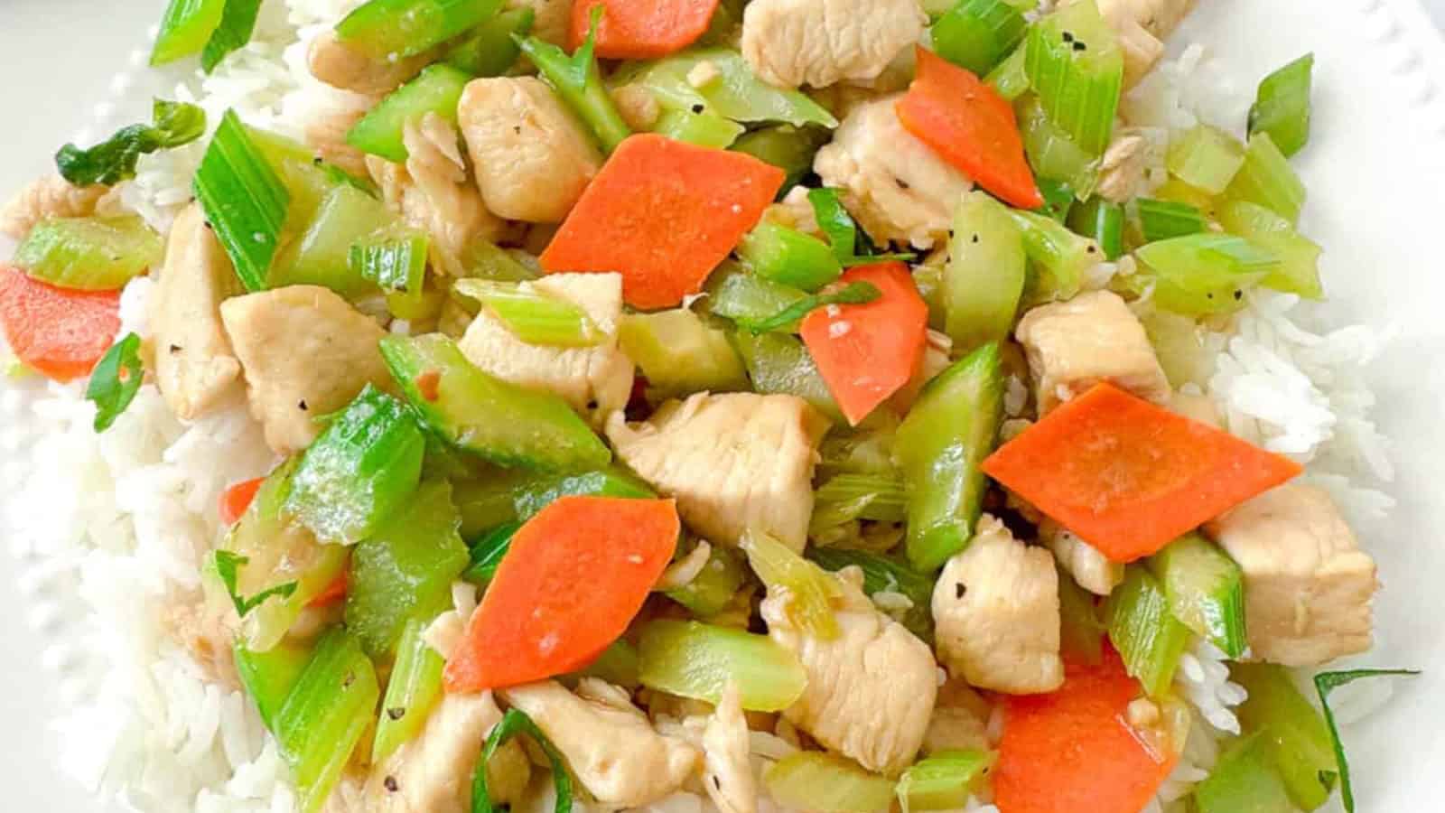 A plate of white rice topped with diced chicken, sliced carrots, celery, and green onions.