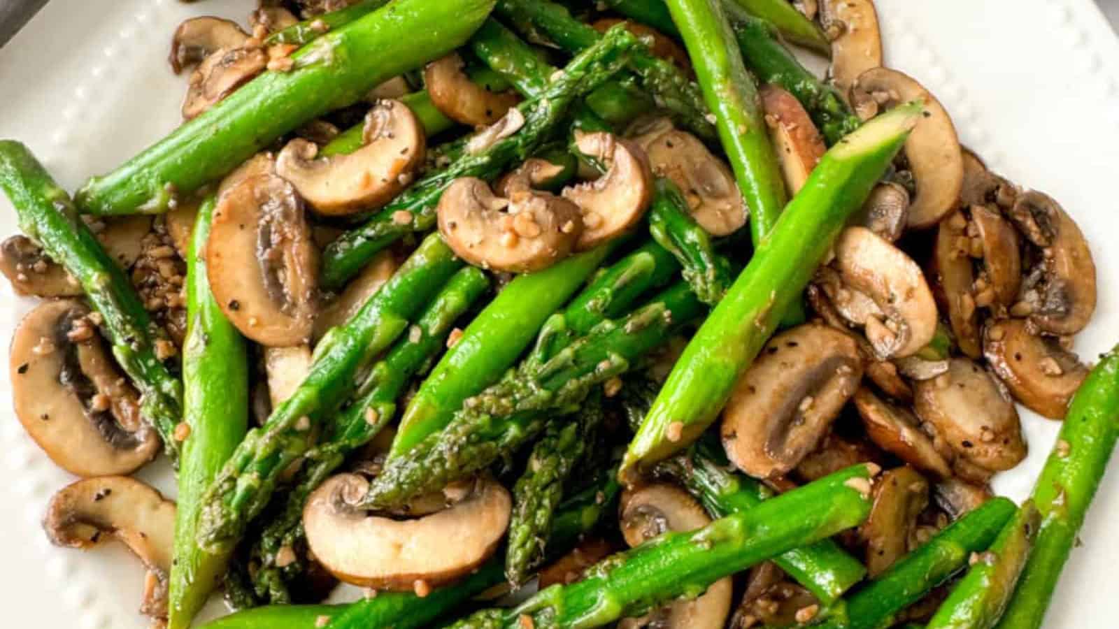 Sautรฉed asparagus and sliced mushrooms seasoned with black pepper and sesame seeds, served on a white plate.