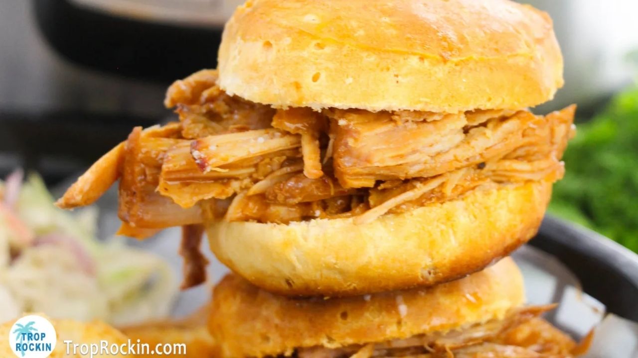 A close-up of two pulled pork sandwiches stacked on top of each other, with shredded pork and barbecue sauce on buns.