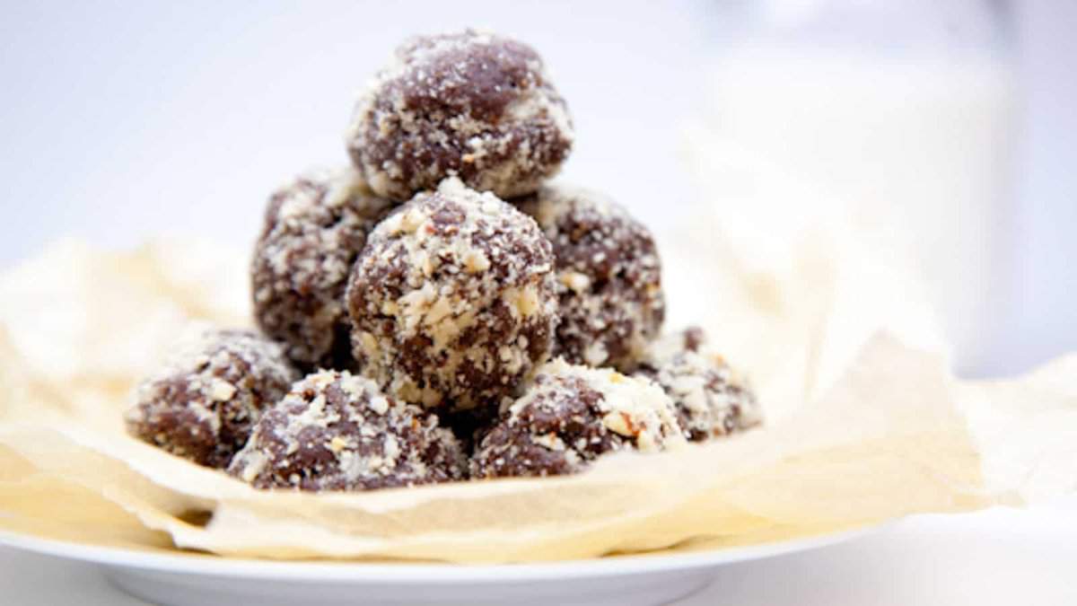 A plate with a pile of round chocolate truffles coated in chopped nuts, placed on crumpled parchment paper.