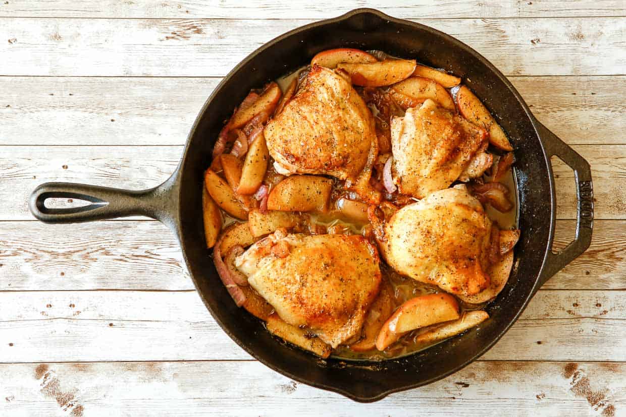 A cast iron skillet with chicken and apples in it.