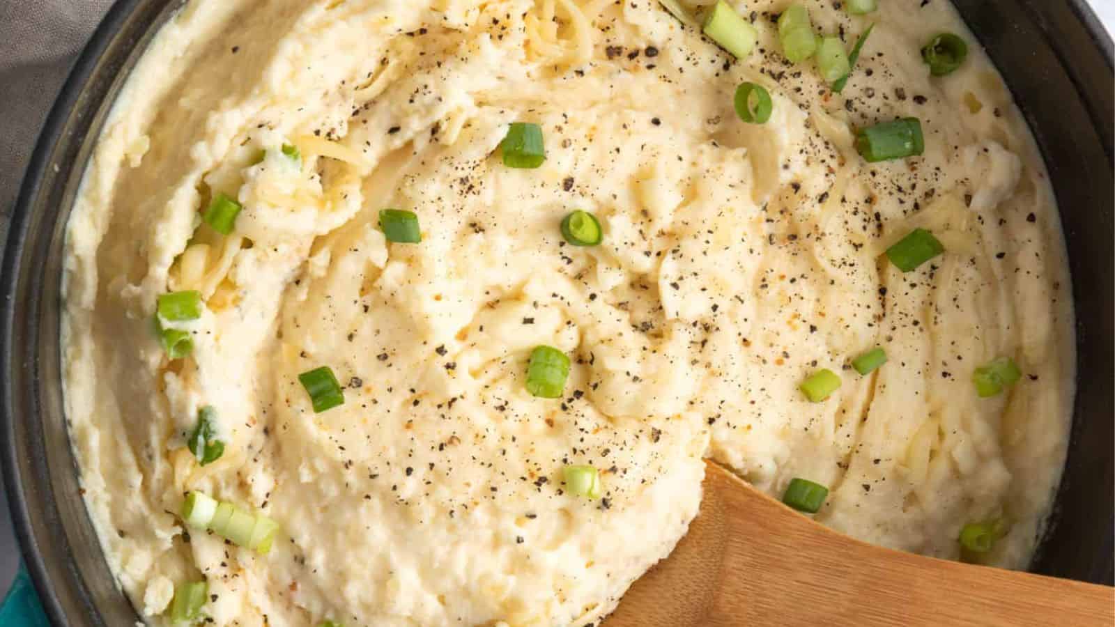 Close up of mashed potatoes in a Dutch oven, with wooden spoon.