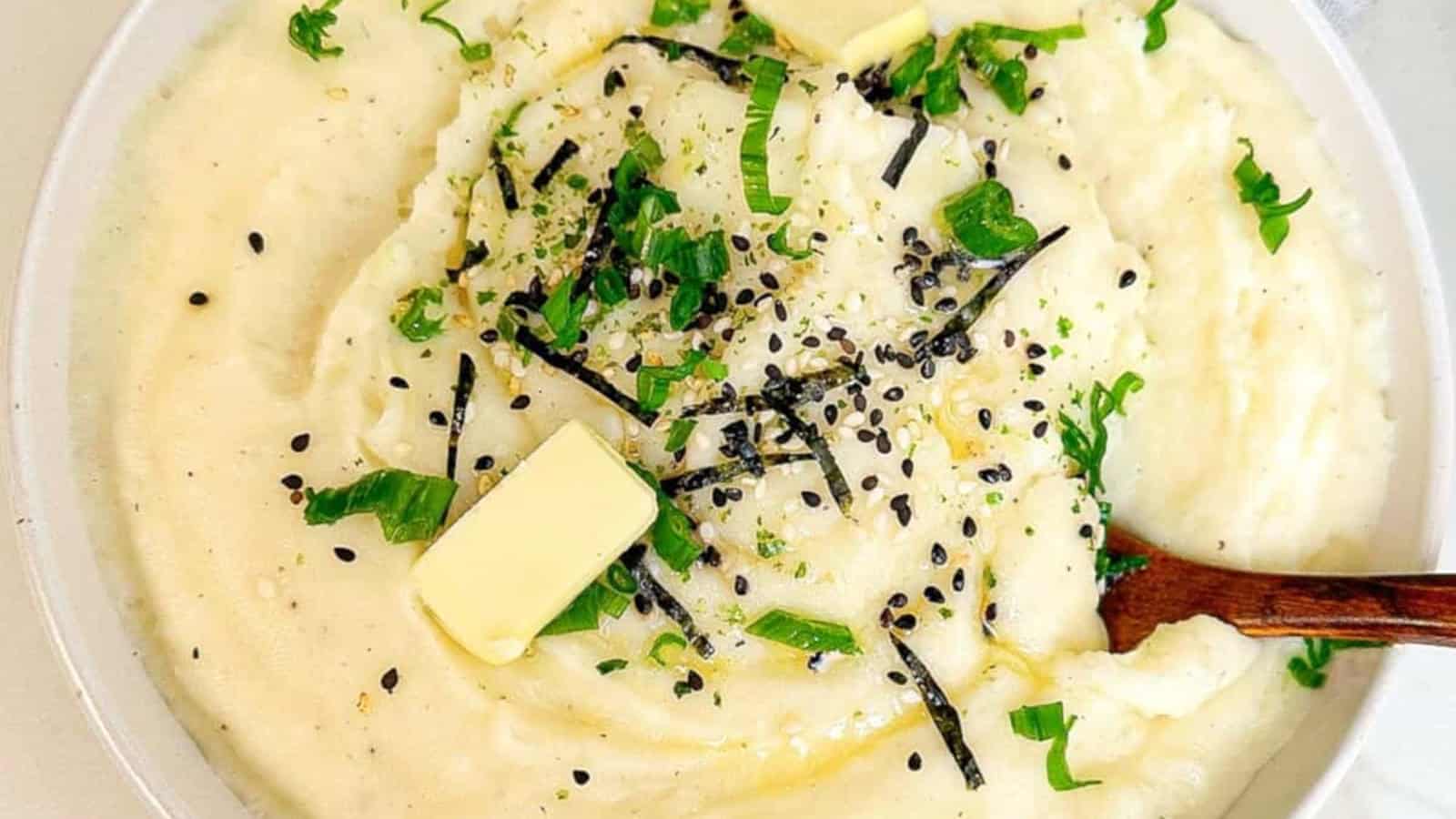A bowl of mashed potatoes topped with butter, chopped green onions, seaweed strips, and black sesame seeds.
