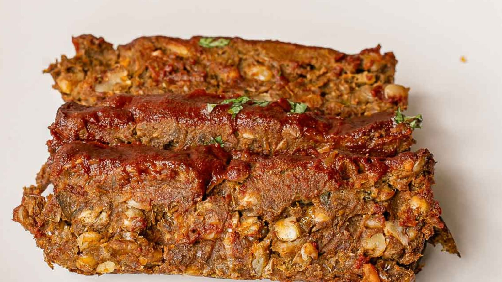 Three slices of lentil loaf topped with tomato sauce are arranged on a plain white plate.
