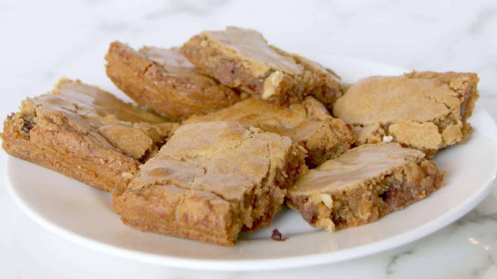 A white plate with several rectangular golden-brown blondies, showing a slightly crisp top and visible nut pieces.