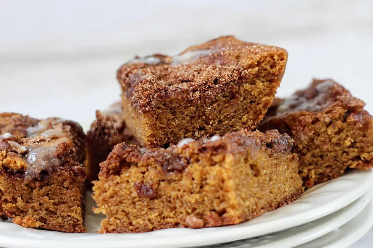 A close-up of several pieces of moist, spiced coffee cake with a crumbly cinnamon topping, stacked on a white plate.