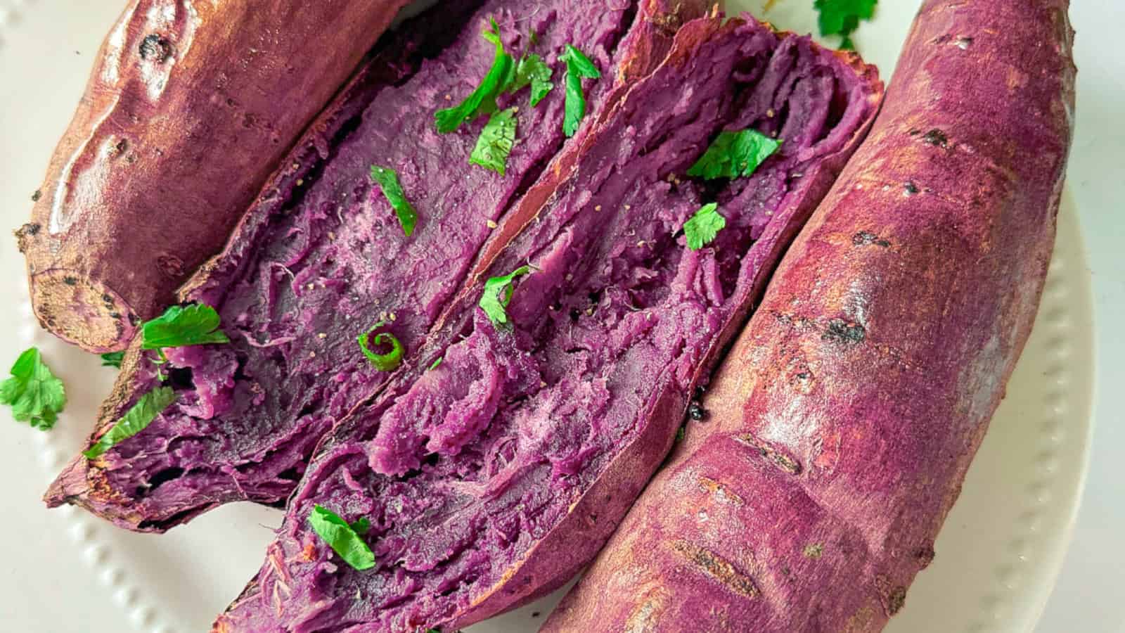 Sweet and creamy oven-roasted purple yams on a white plate with green onions.