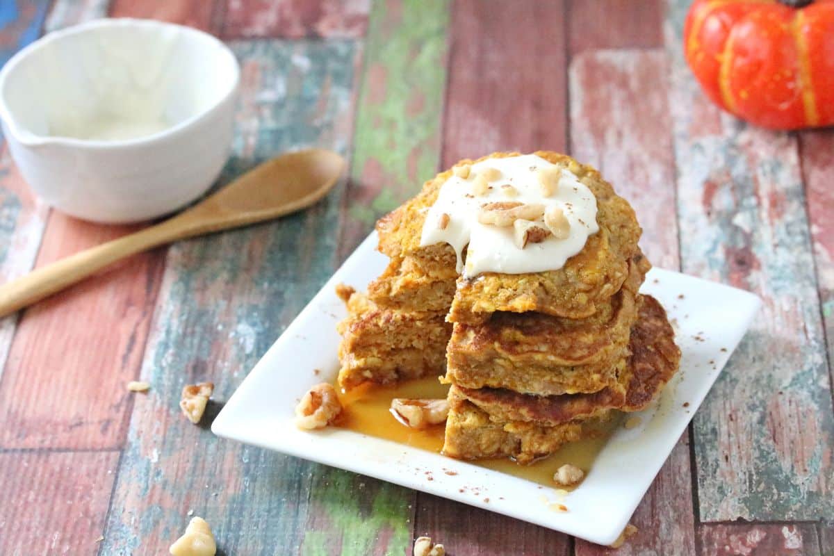 A stack of pumpkin pancakes with whipped cream and pecans.