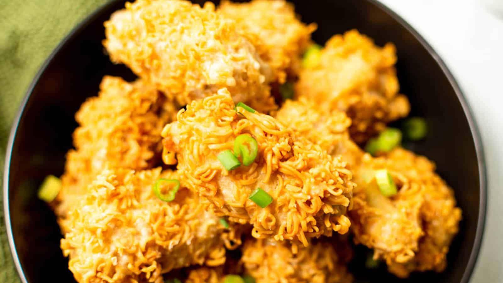 Hand reaching into a bowl of ramen fried chicken pieces.