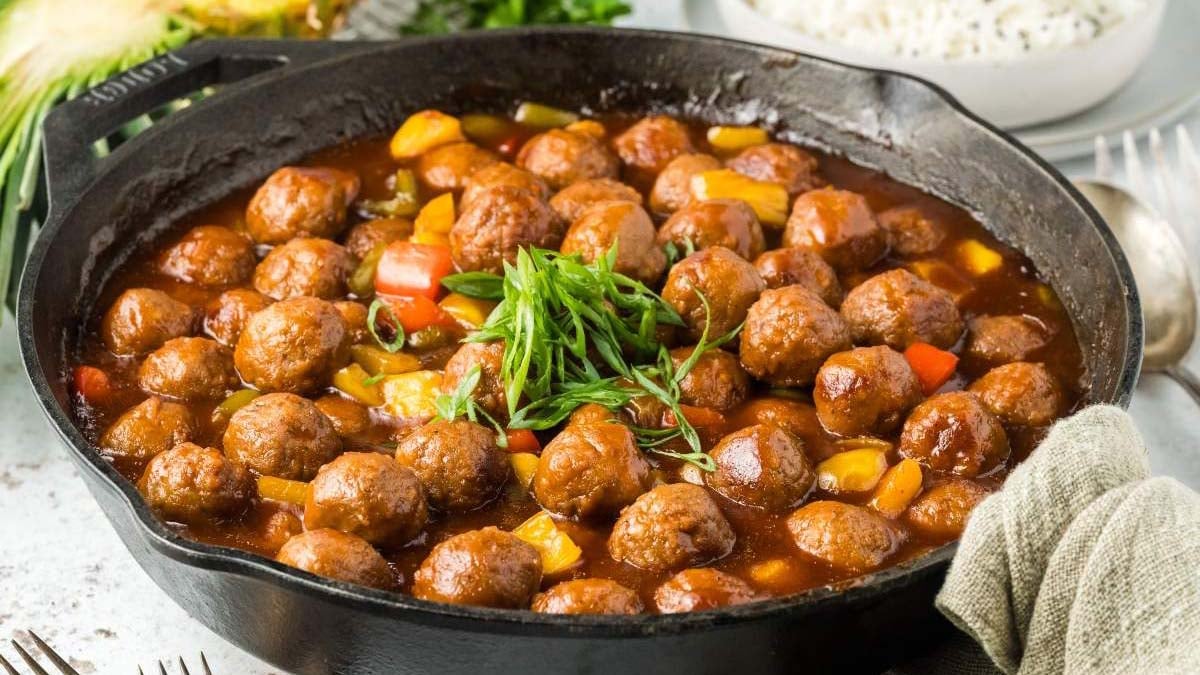 A cast iron skillet filled with meatballs in a brown sauce, garnished with chopped green onions and mixed with diced vegetables.