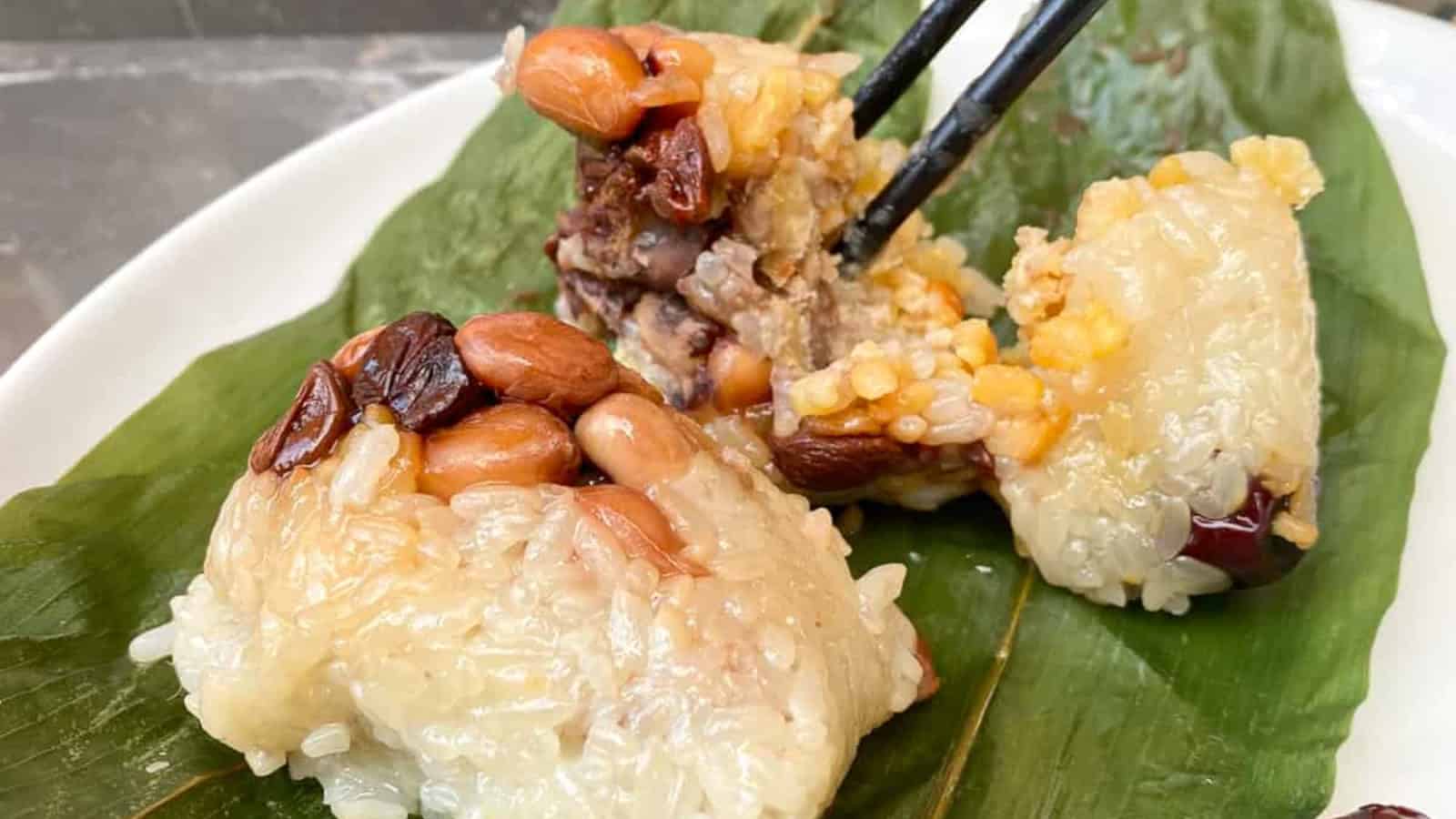 Traditional Chinese sticky rice dumplings wrapped in bamboo leaves on a white plate.