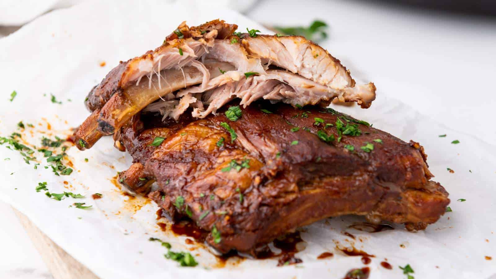 Close-up of cooked baby back ribs on parchment, garnished with chopped parsley.