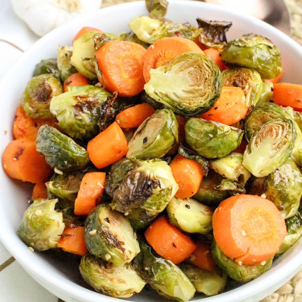 A white bowl filled with roasted Brussels sprouts and sliced carrots, lightly browned and seasoned.