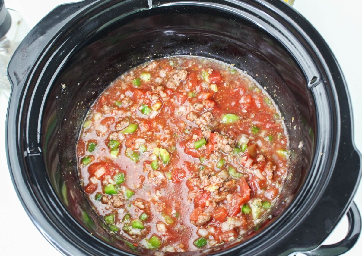 A slow cooker filled with a mixture of chopped vegetables, ground meat, and tomato sauce.
