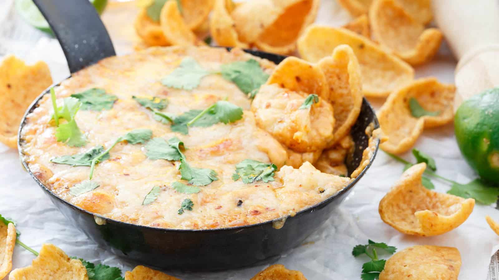 A skillet filled with cheesy dip topped with cilantro, surrounded by corn chips for dipping.