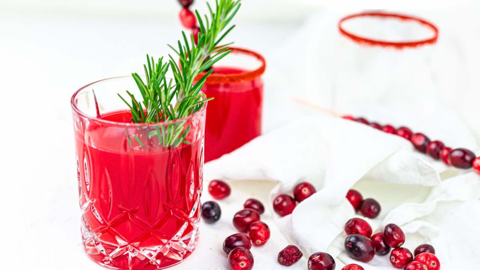 A glass of red liquid with a sprig of rosemary on top.