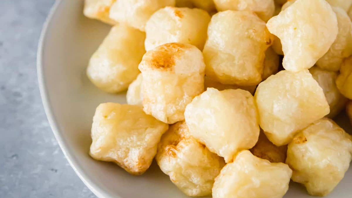 A white bowl filled with golden, puffy fried cheese curds on a gray surface.
