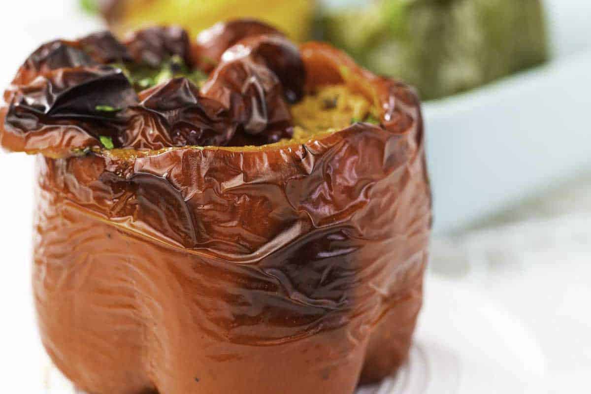 A close-up of a cooked stuffed red bell pepper with a wrinkled, roasted skin, sitting on a white surface.