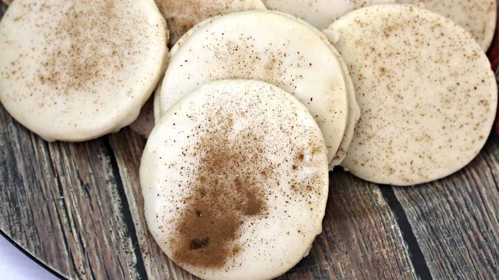 A plate of round, white cookies topped with a dusting of cinnamon, displayed on a wooden surface.