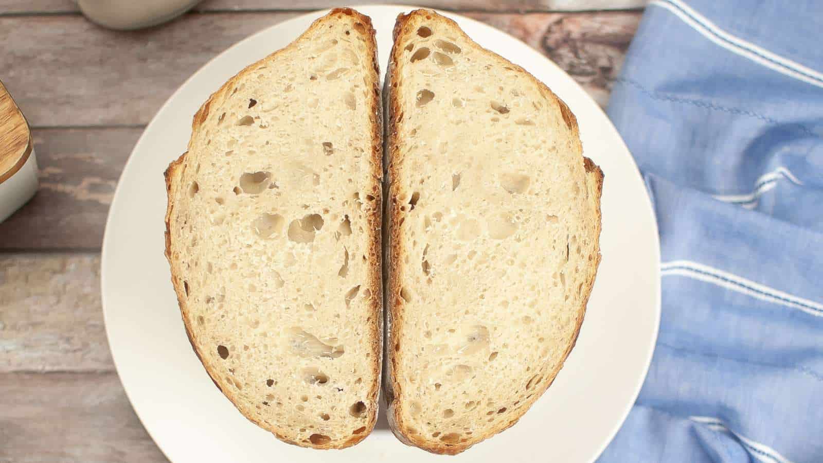 Two slices of rustic bread are placed side by side on a white plate, viewed from above, with a blue cloth visible to the right.