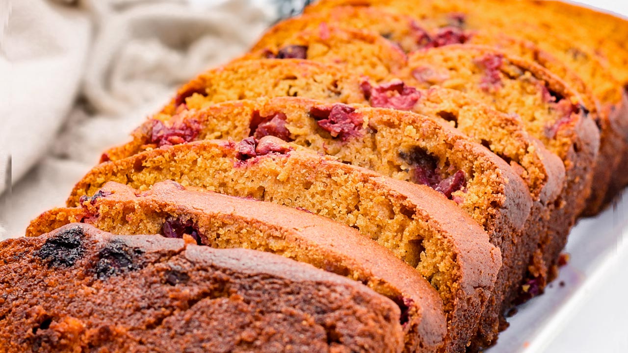 Sliced cranberry bread loaf arranged on a white plate, showing its moist texture and visible cranberry pieces.