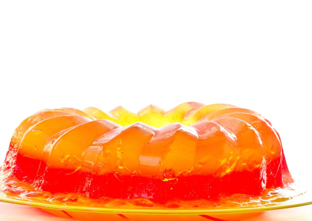 A round, two-layer orange and red gelatin dessert sits on a yellow glass plate against a white background.