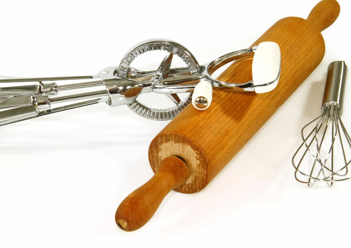 A wooden rolling pin, a metal hand mixer, and a small wire whisk are placed on a white background.