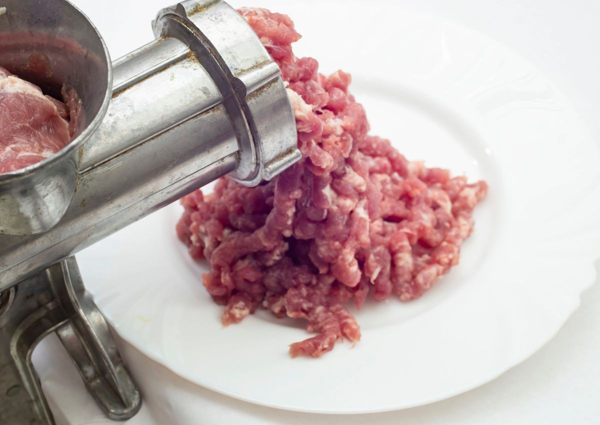 Ground meat coming out of a metal meat grinder onto a white plate.