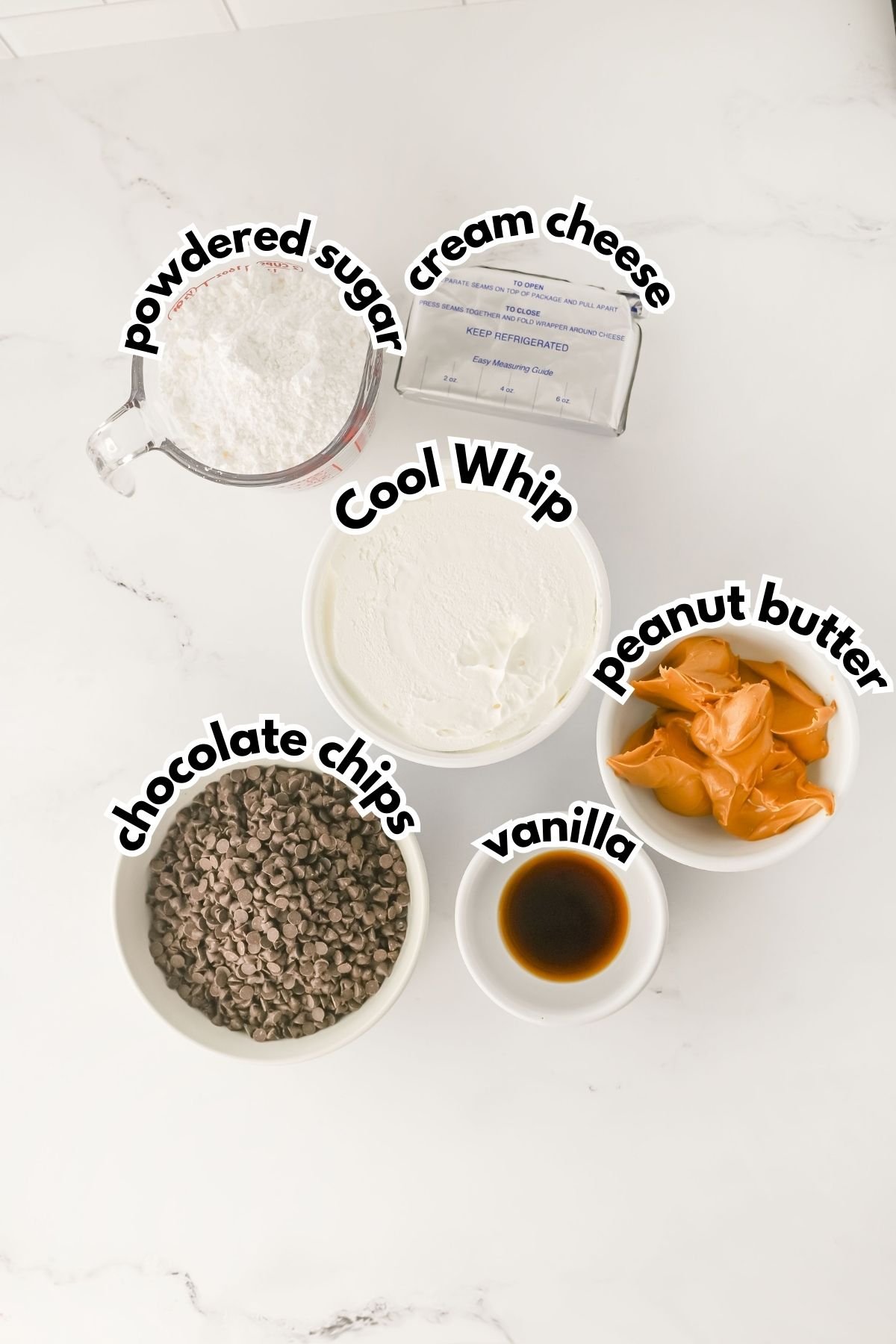 Five labeled bowls containing powdered sugar, cream cheese, Cool Whip, chocolate chips, vanilla, and peanut butter on a white countertop.