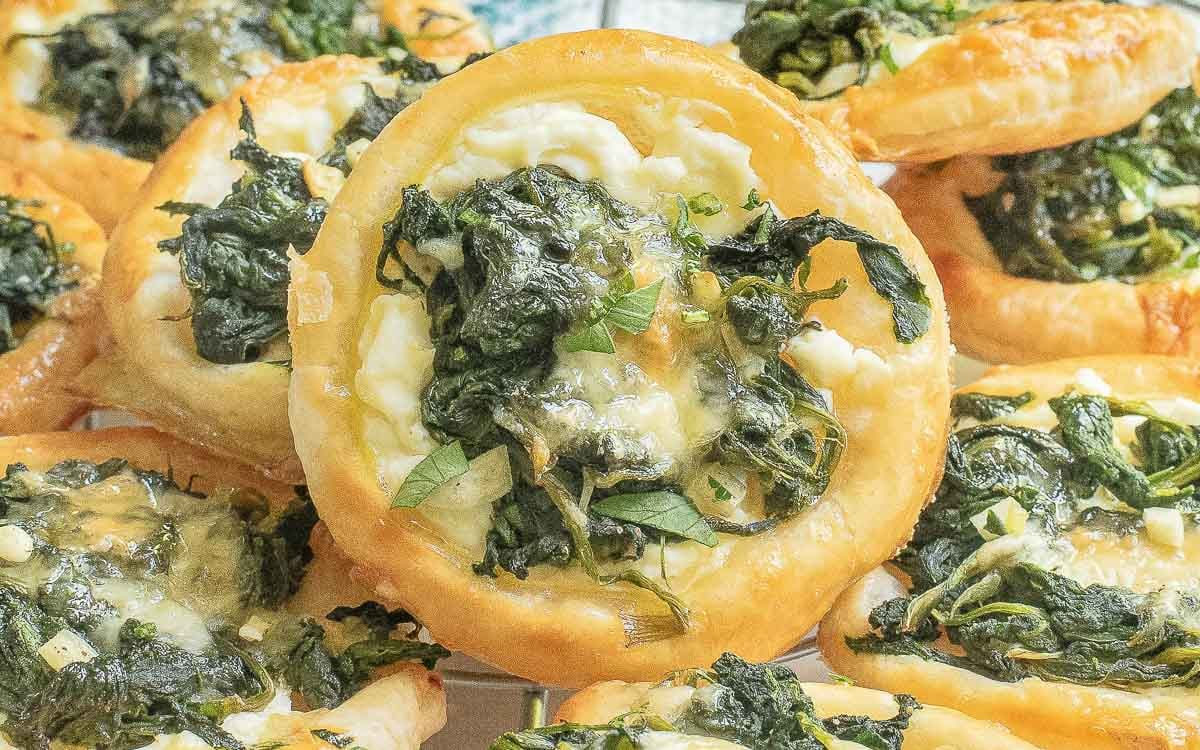 Close-up of several baked puff pastry rounds topped with spinach, cheese, and herbs.