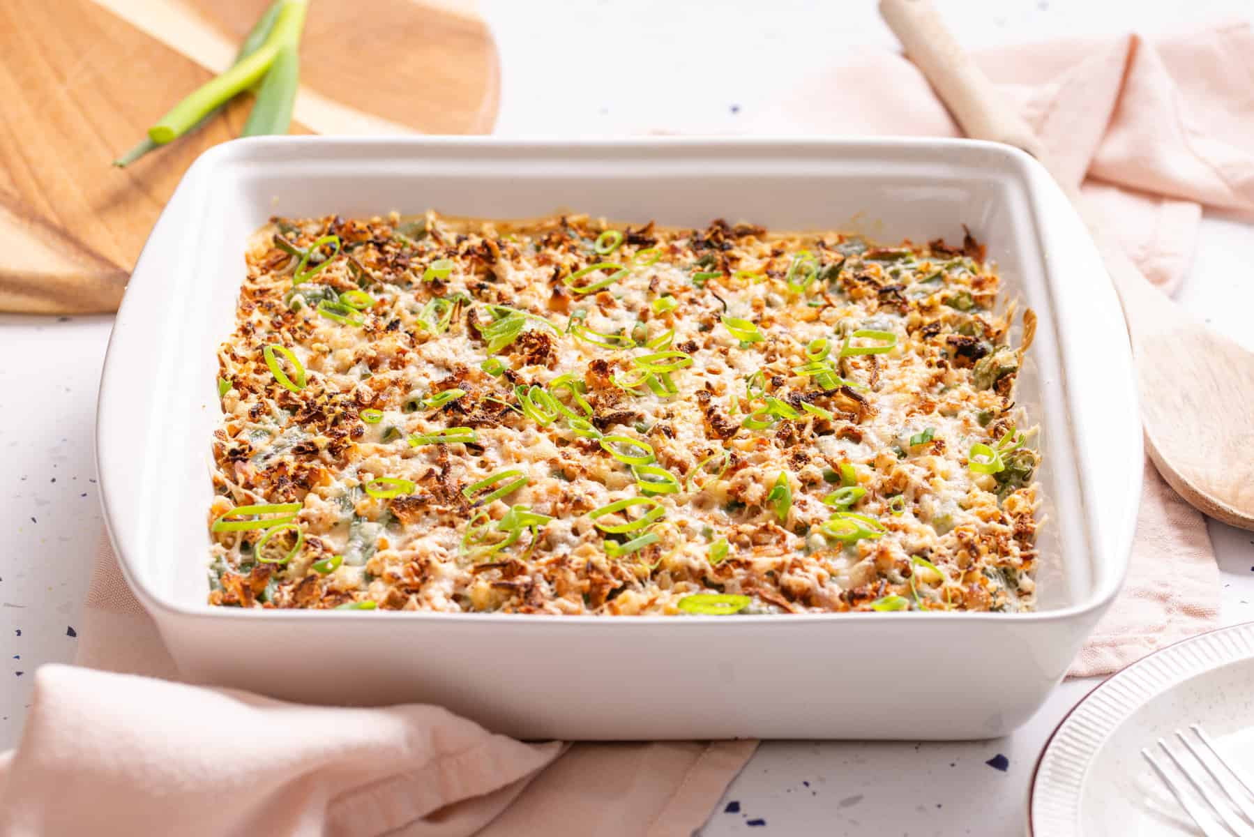 A Green Bean Casserole with Cream Cheese topped with a golden-brown crust and garnished with sliced green onions.