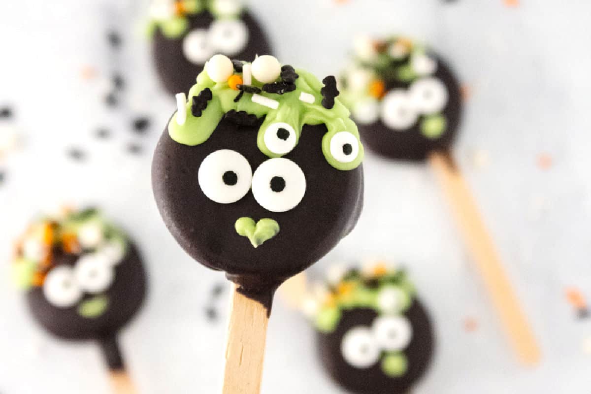 Halloween-themed cake pops with googly eyes and colorful sprinkles on a marble surface.