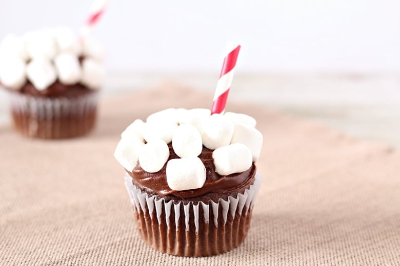 Chocolate cupcake topped with chocolate frosting, mini marshmallows, and a red-and-white striped paper straw, placed on a burlap surface.