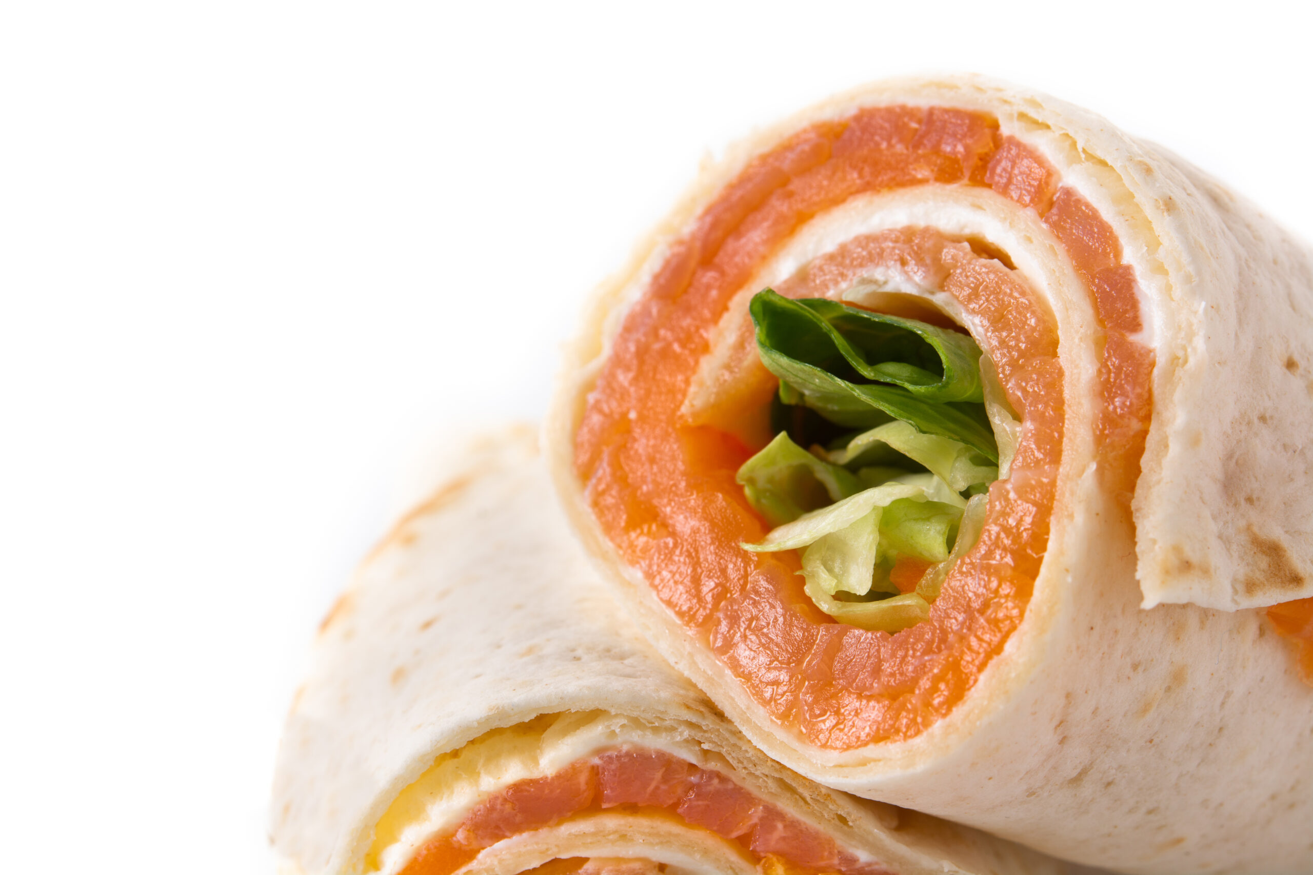 Close-up of a tortilla wrap filled with slices of smoked salmon and green leafy vegetables, against a white background.
