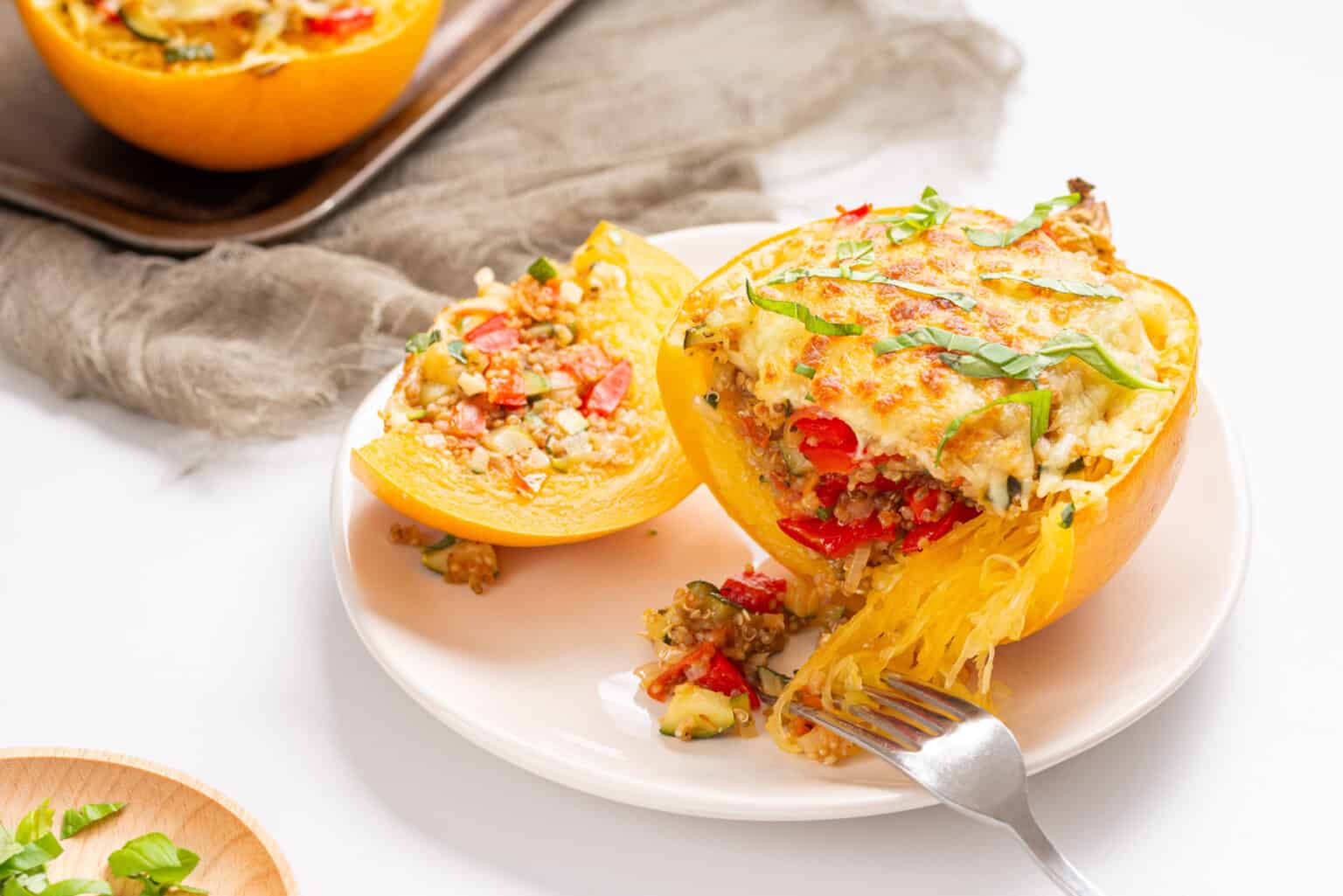 An image of two stuffed spaghetti squashes on a white plate with a fork slicing a part of one of the squashes.