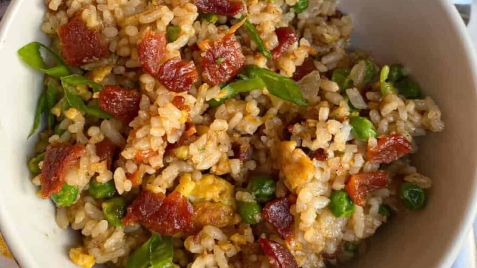 Bacon fried rice in a white bowl with green onions on the top.