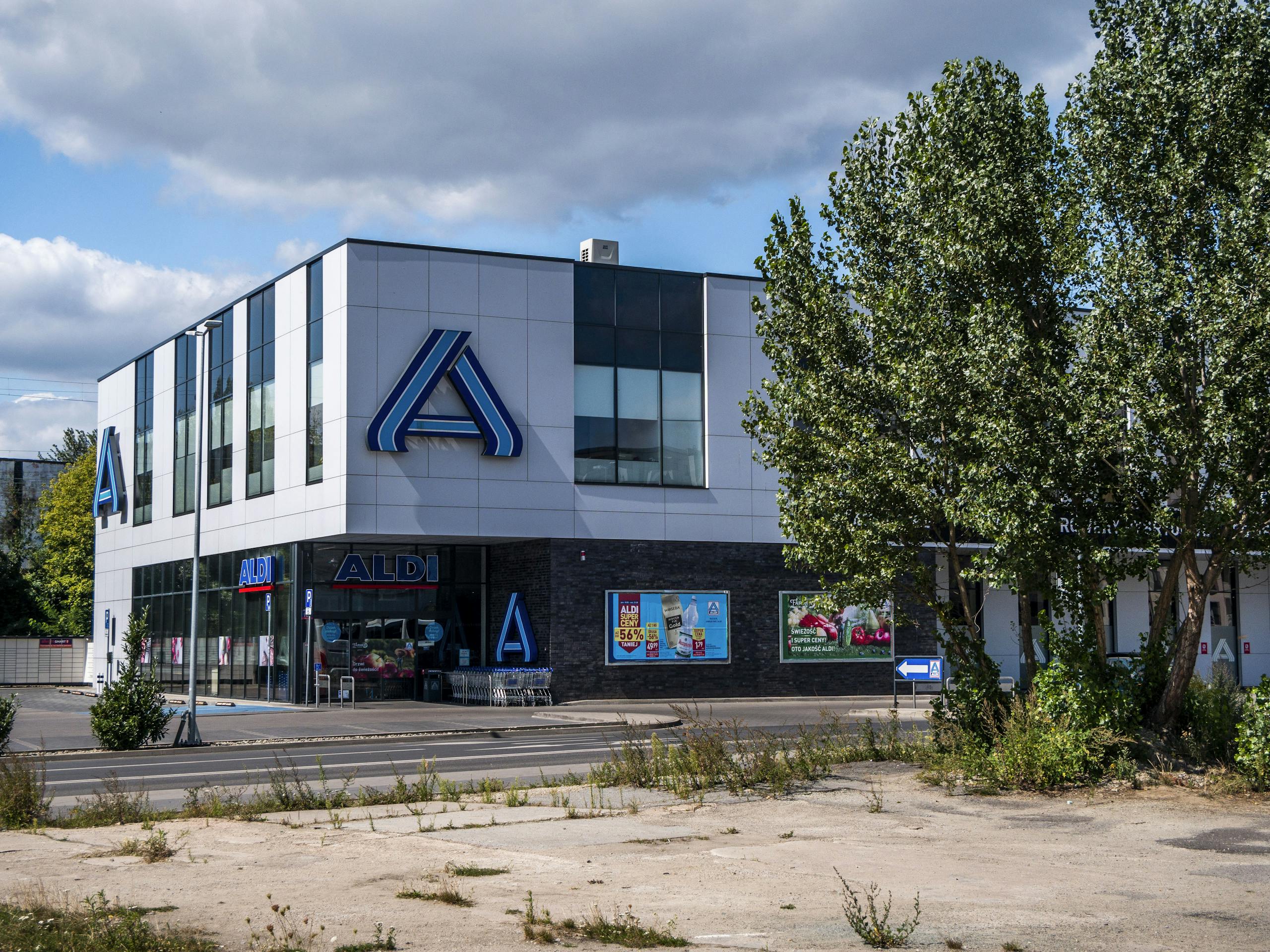 Blue and white modern Aldi store exterior surrounded by green trees under a clear sky