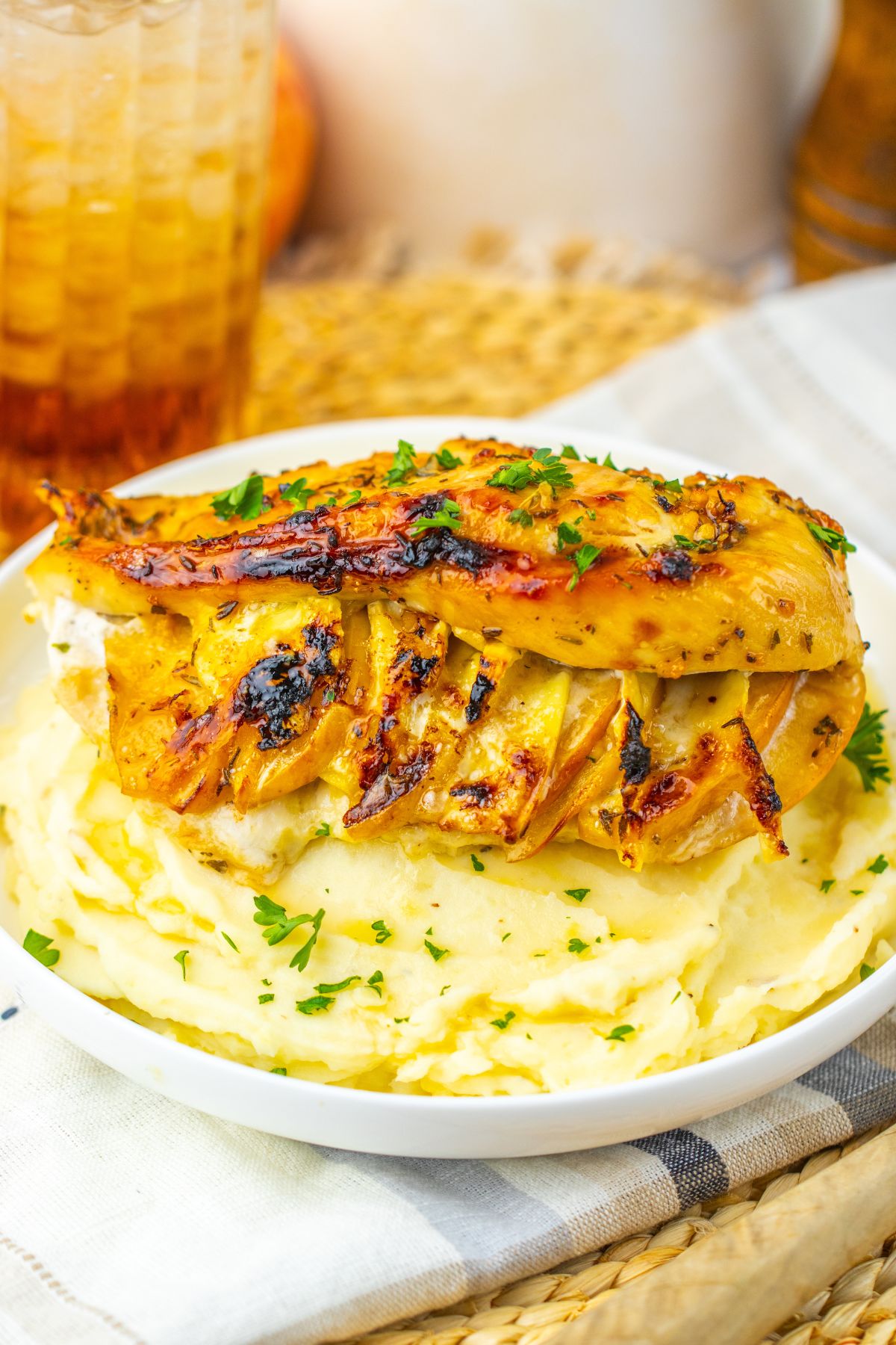 Grilled chicken breast sliced on top of a mound of mashed potatoes, garnished with chopped parsley, served on a white plate.
