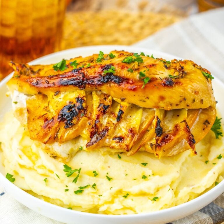 Grilled chicken breast stuffed with cheese sits on a mound of mashed potatoes, garnished with chopped parsley.