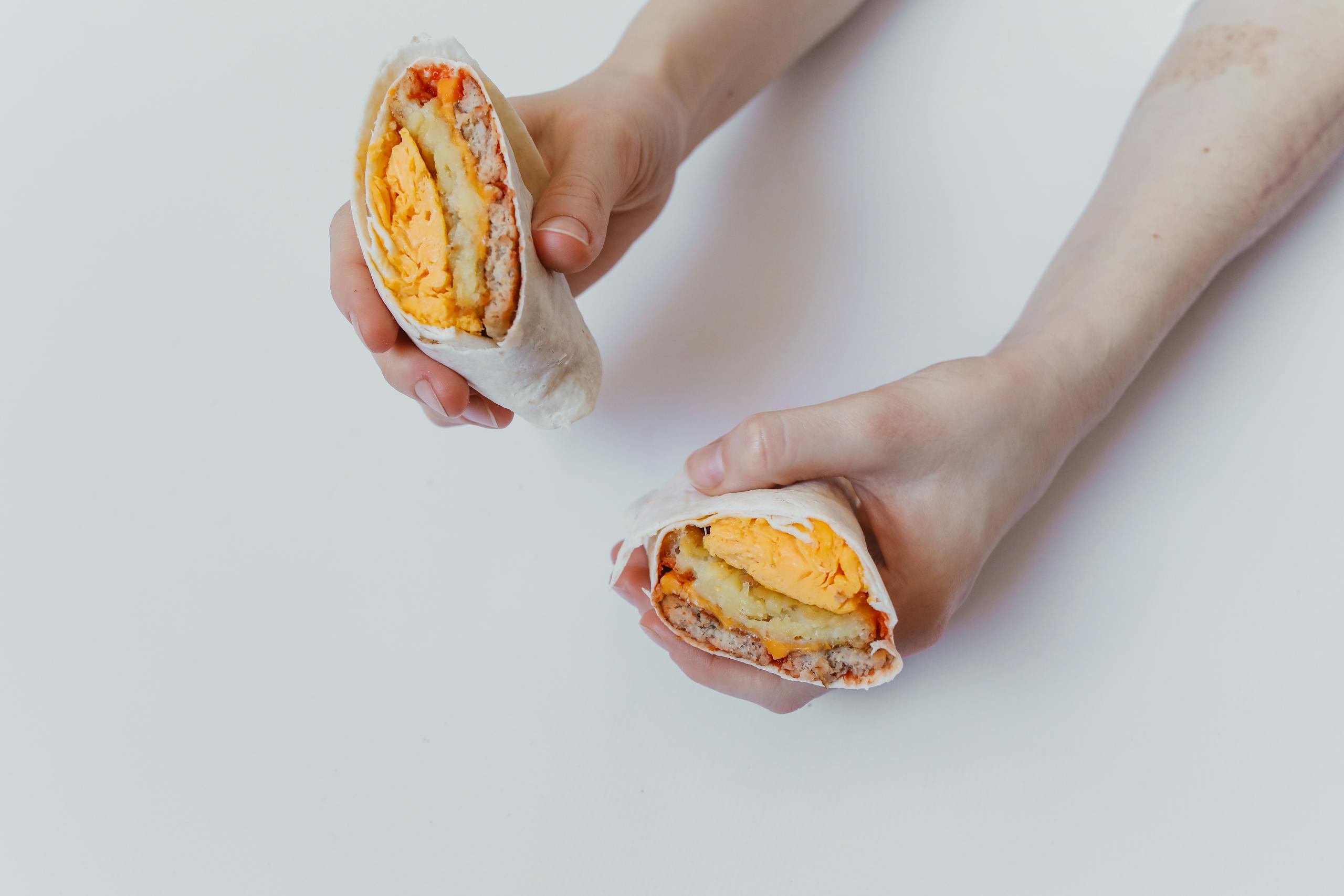 Close-up of hands holding a cut breakfast burrito with eggs, cheese, and meat.