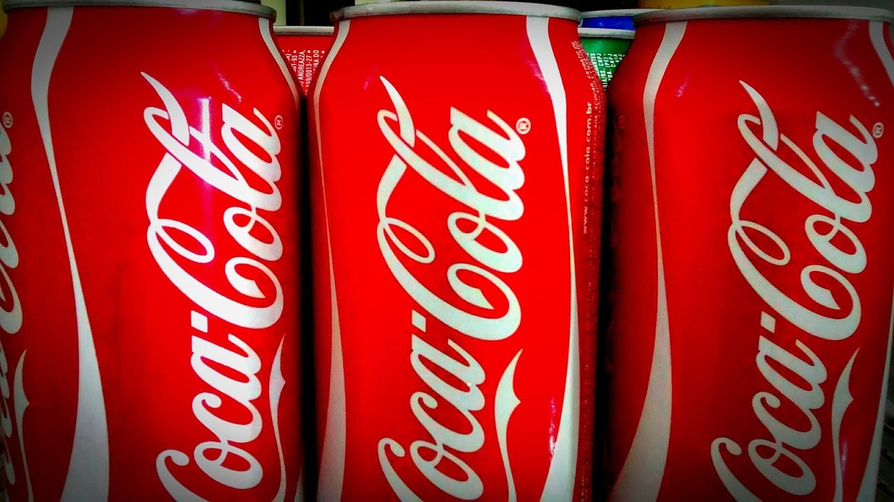 Several red Coca-Cola cans are lined up closely together, displaying the white Coca-Cola logo prominently.