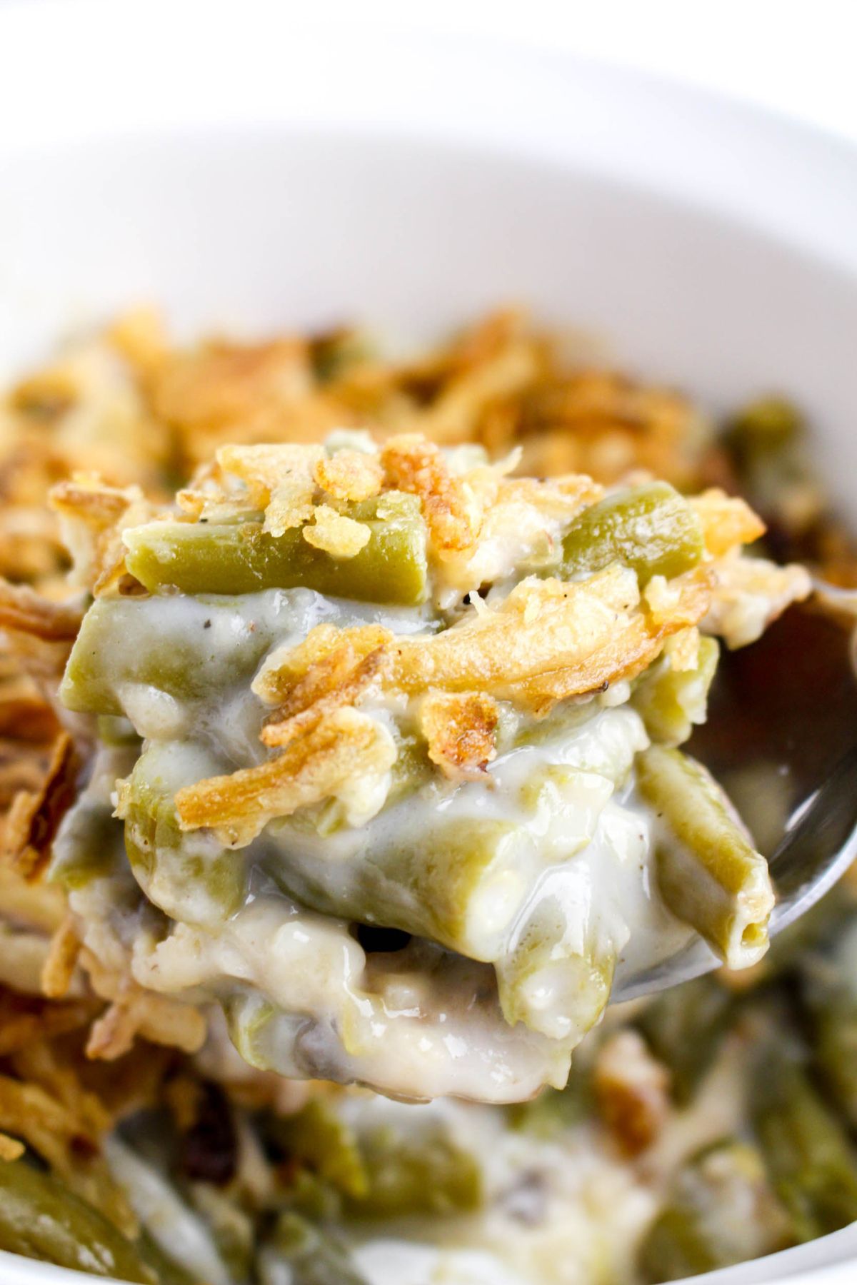 A close-up of a spoonful of green bean casserole topped with crispy fried onions in a white bowl.