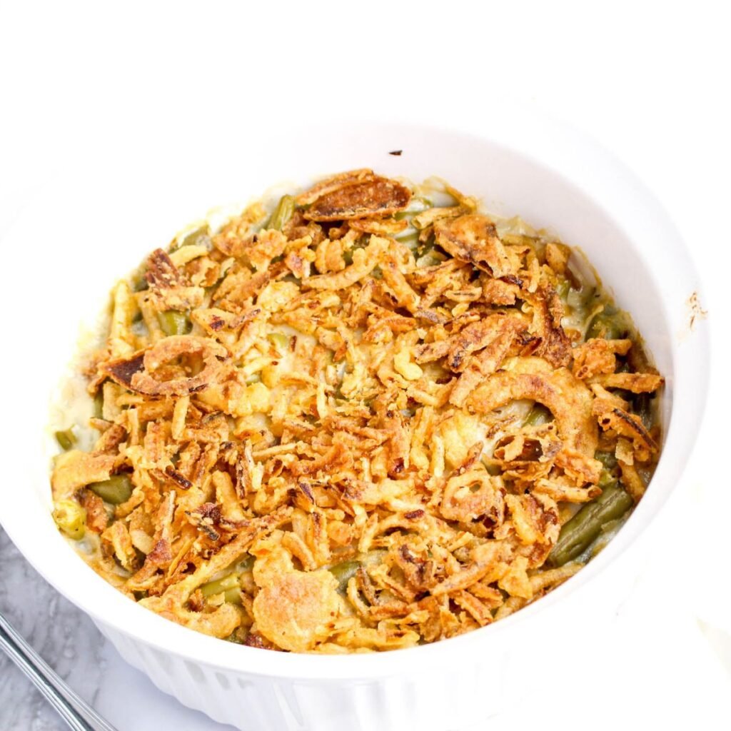 A white casserole dish filled with green bean casserole topped with crispy fried onions.