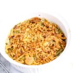 A white casserole dish filled with green bean casserole topped with crispy fried onions.