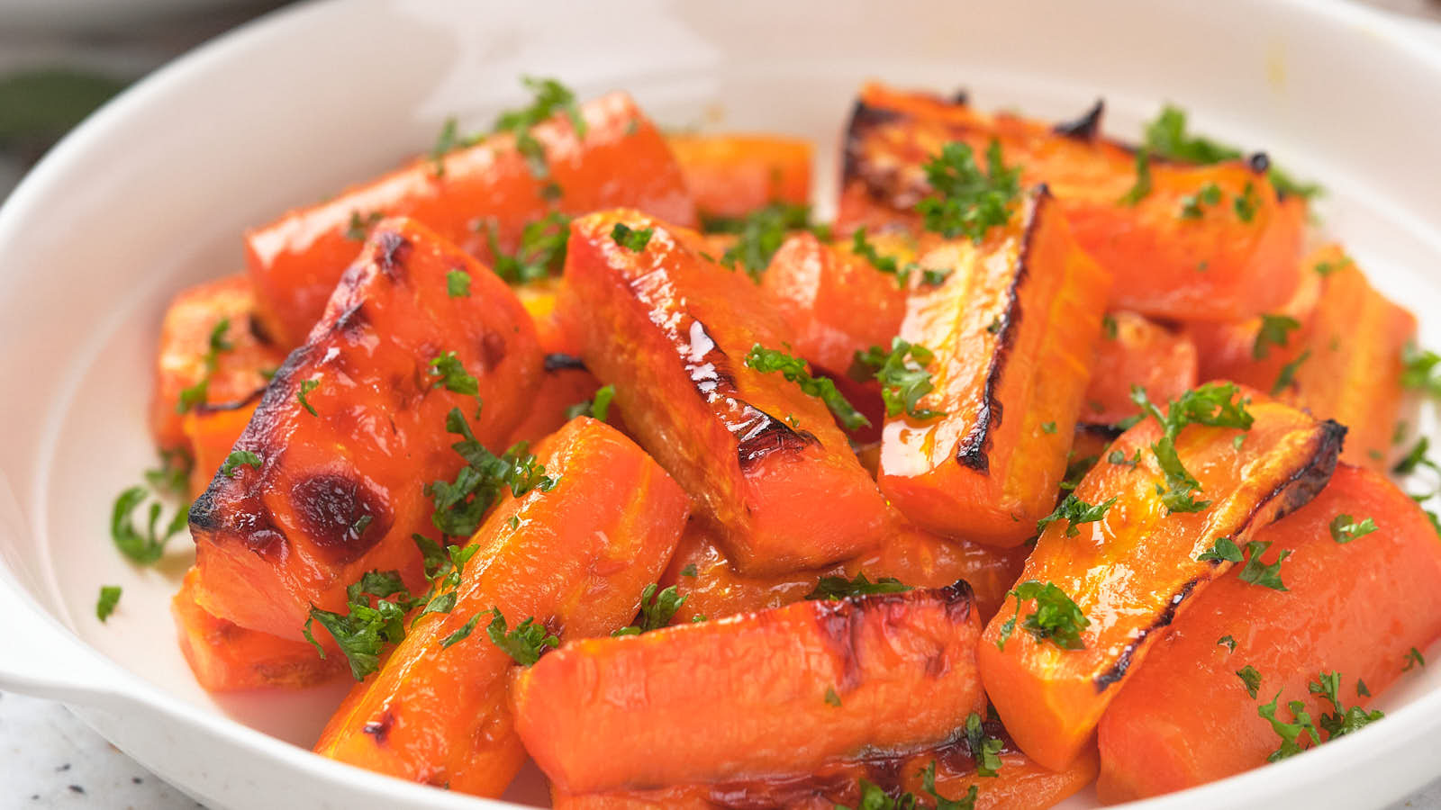 A white dish filled with roasted carrot pieces garnished with chopped parsley.