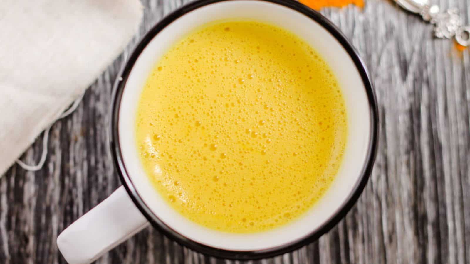 A white mug filled with frothy yellow turmeric milk sits on a gray wooden surface.